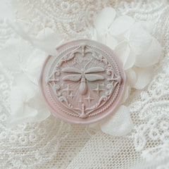 "Firefly Whisper" wax seal featuring an intricately designed seal with a delicate firefly motif and the words "Wish You Well." The seal is beautifully displayed on a background of soft white lace and delicate hydrangea petals, creating an elegant and ethereal atmosphere. This unique seal adds a touch of sophistication to letters or invitations. Crafted from high-quality materials.