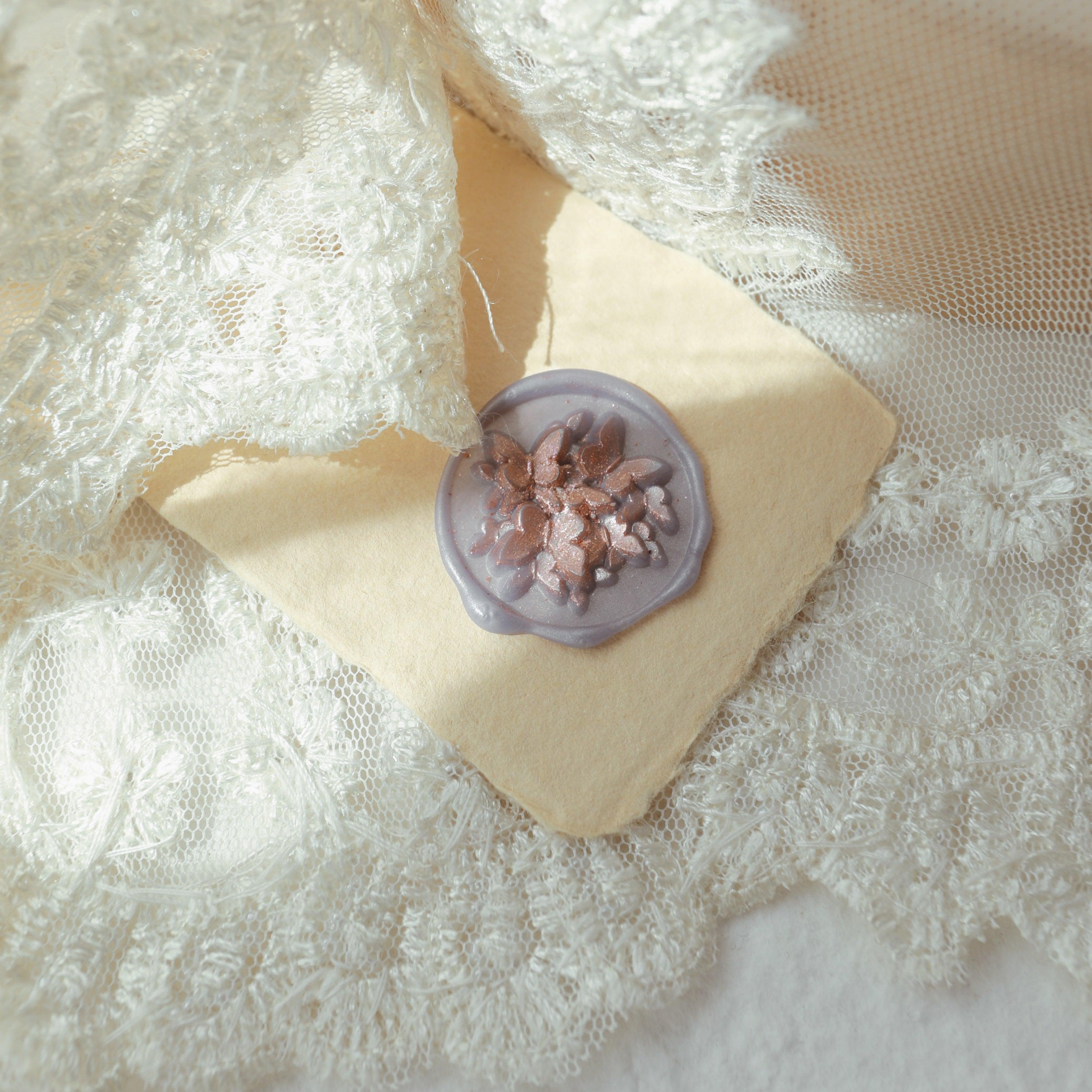 A twilight blue wax seal with an intricate floral relief design, placed on a beige card, surrounded by luxurious white lace fabric. The sheen of the wax seal combined with the delicate texture of the lace creates a romantic and elegant atmosphere, perfect for decorating wedding invitations or exquisite crafts.