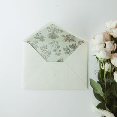 The Limerence Seals "Textures of Time" envelope features an elegant design with a textured exterior and a beautifully illustrated botanical print lining inside. The envelope is accompanied by a bouquet of delicate, blush pink roses on the right side, creating a harmonious and graceful composition that embodies elegance and sophistication.