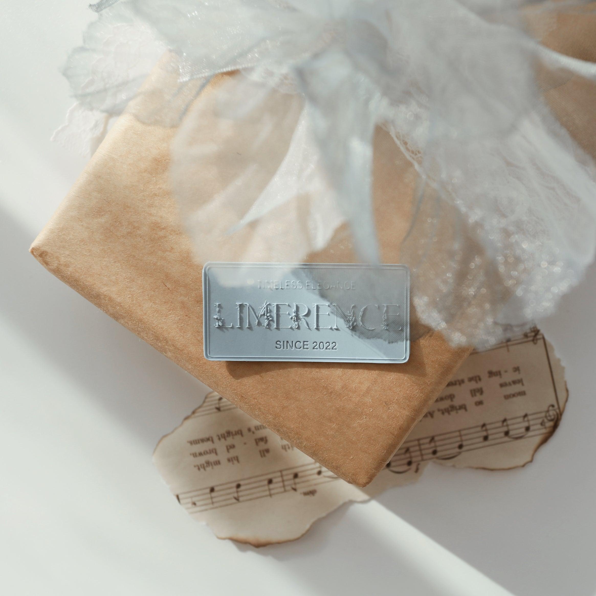 A beautifully wrapped gift adorned with a denim blue Limerence Seals label embossed with "TIMELESS ELEGANCE - LIMERENCE - SINCE 2022." The package features delicate lace ribbon and vintage sheet music, creating a harmonious blend of elegance and nostalgia, perfect for memorable occasions and sophisticated gifting.