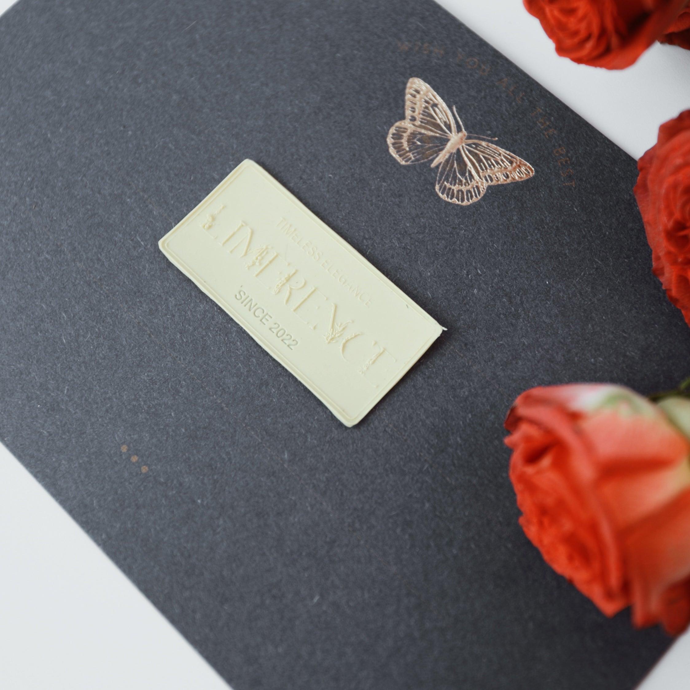 Elegant presentation of a ginger yellow Limerence Seals label embossed with "TIMELESS ELEGANCE - LIMERENCE - SINCE 2022" on a dark envelope featuring a delicate butterfly design. The scene is complemented by vibrant red roses, showcasing the brand's dedication to timeless beauty and refined aesthetics, perfect for creating sophisticated invitations and gifts.