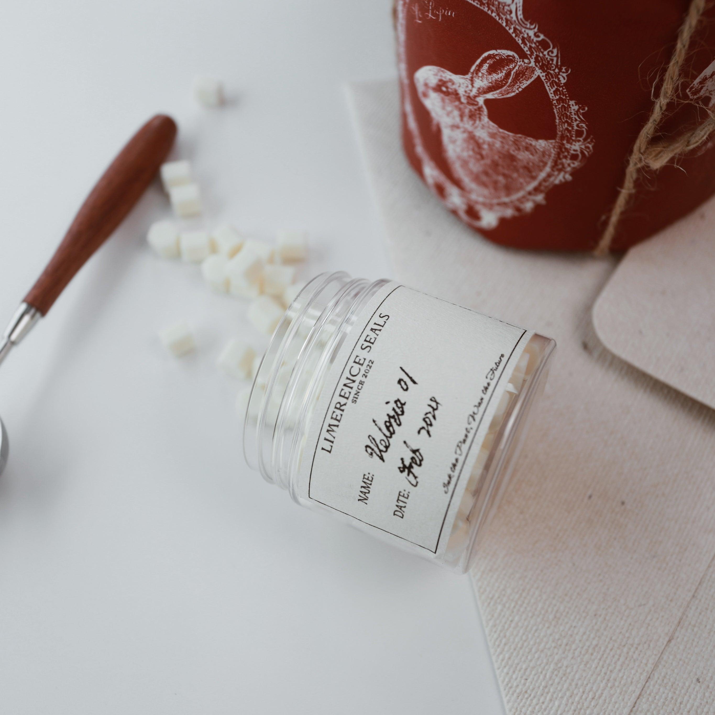 A jar of Veloria handmade sealing wax beads in light yellow by Limerence Seals, with some beads scattered on a white surface. The scene includes a wax seal stamp tool and decorative packaging featuring a rabbit illustration, highlighting the charm and creativity of the product for DIY projects and personalizing gifts.