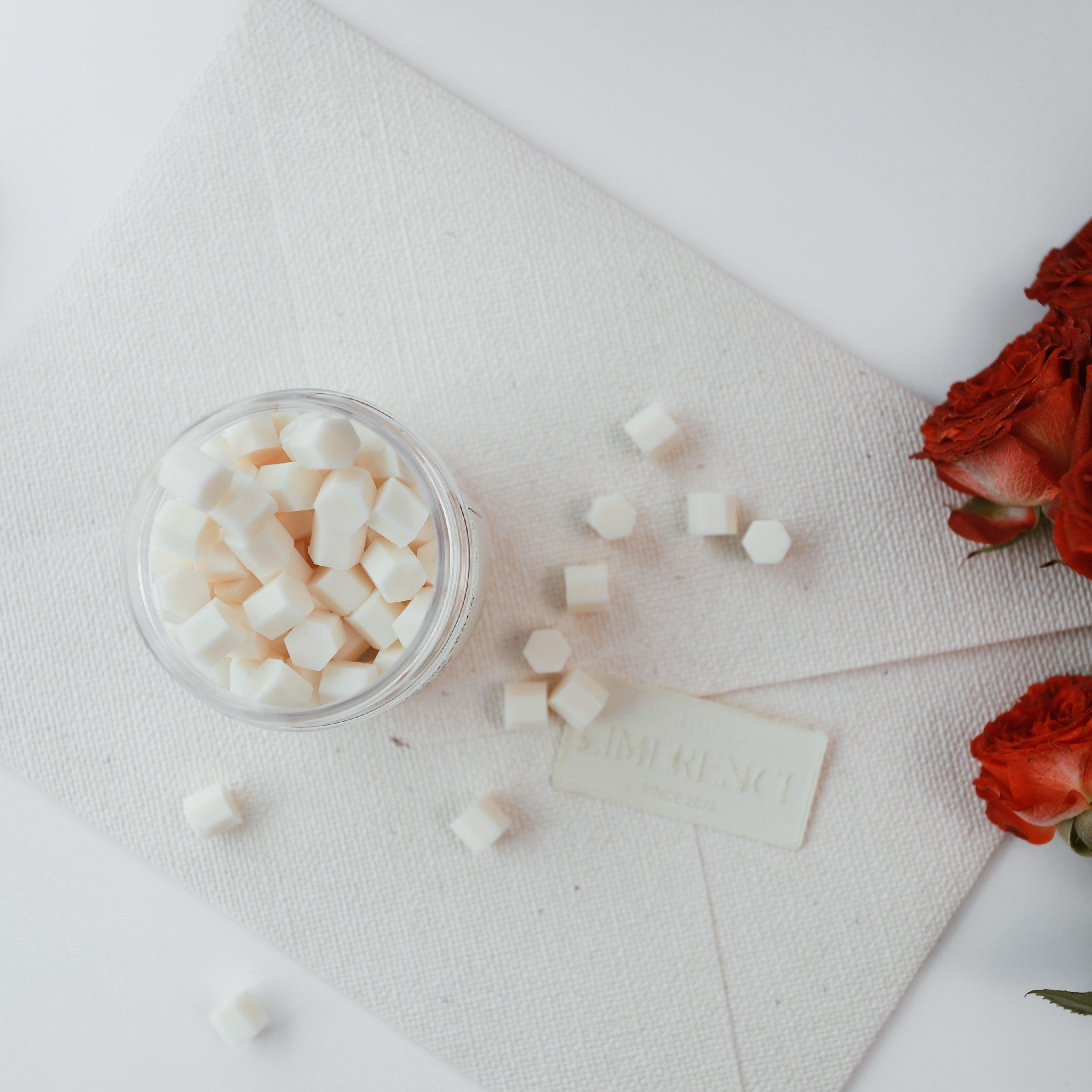 Top view of a jar filled with light yellow Veloria handmade sealing wax beads by Limerence Seals, surrounded by scattered beads on a textured fabric surface. Nearby is an elegant envelope sealed with a matching wax seal and vibrant red roses, showcasing the product's versatility for enhancing special occasions and adding a touch of elegance to invitations.