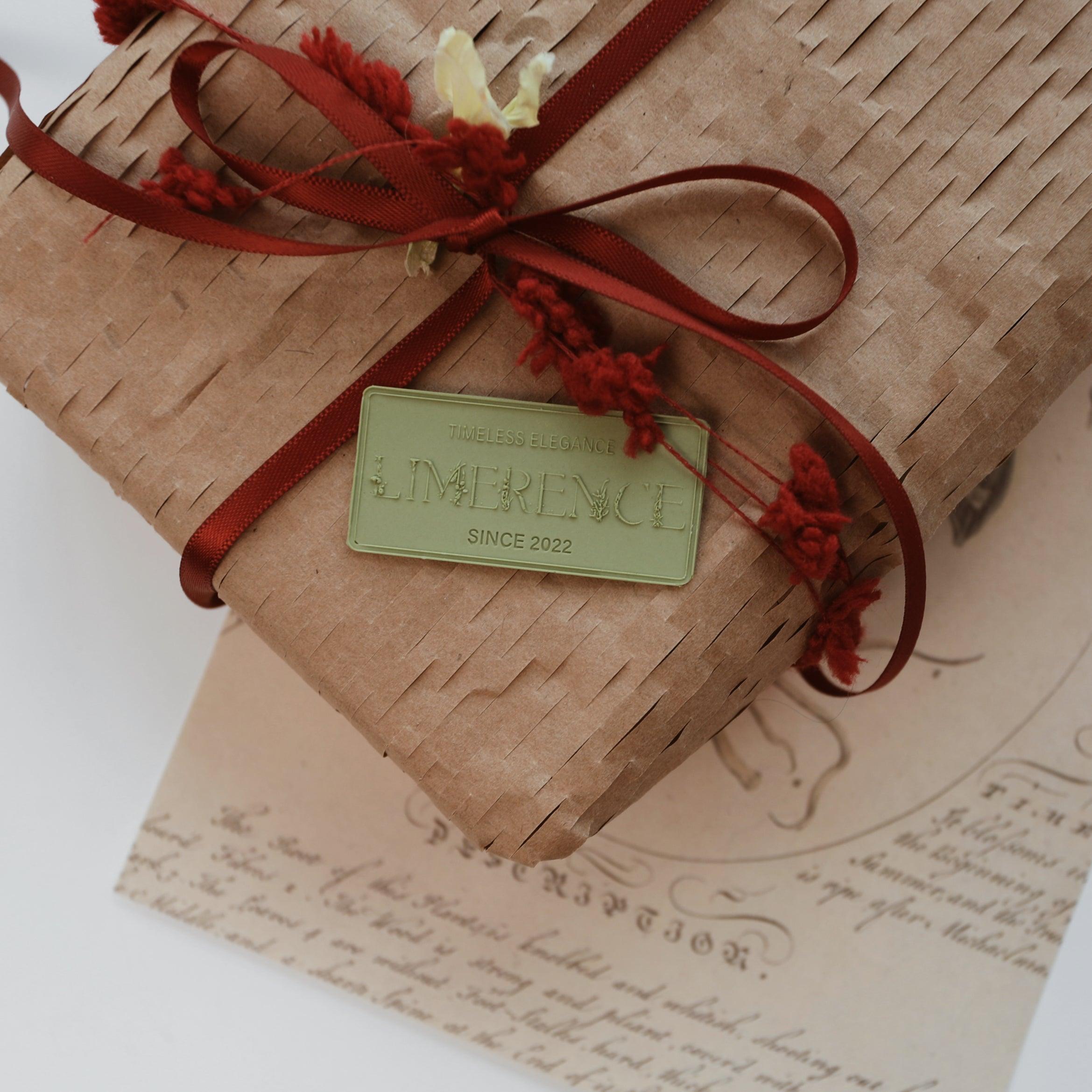 A beautifully wrapped gift featuring a matcha green Limerence Seals label embossed with "TIMELESS ELEGANCE - LIMERENCE - SINCE 2022," tied with a red ribbon bow. The rustic brown paper and vintage script background add a charming touch of elegance, making it ideal for sophisticated gift presentations and themed events.