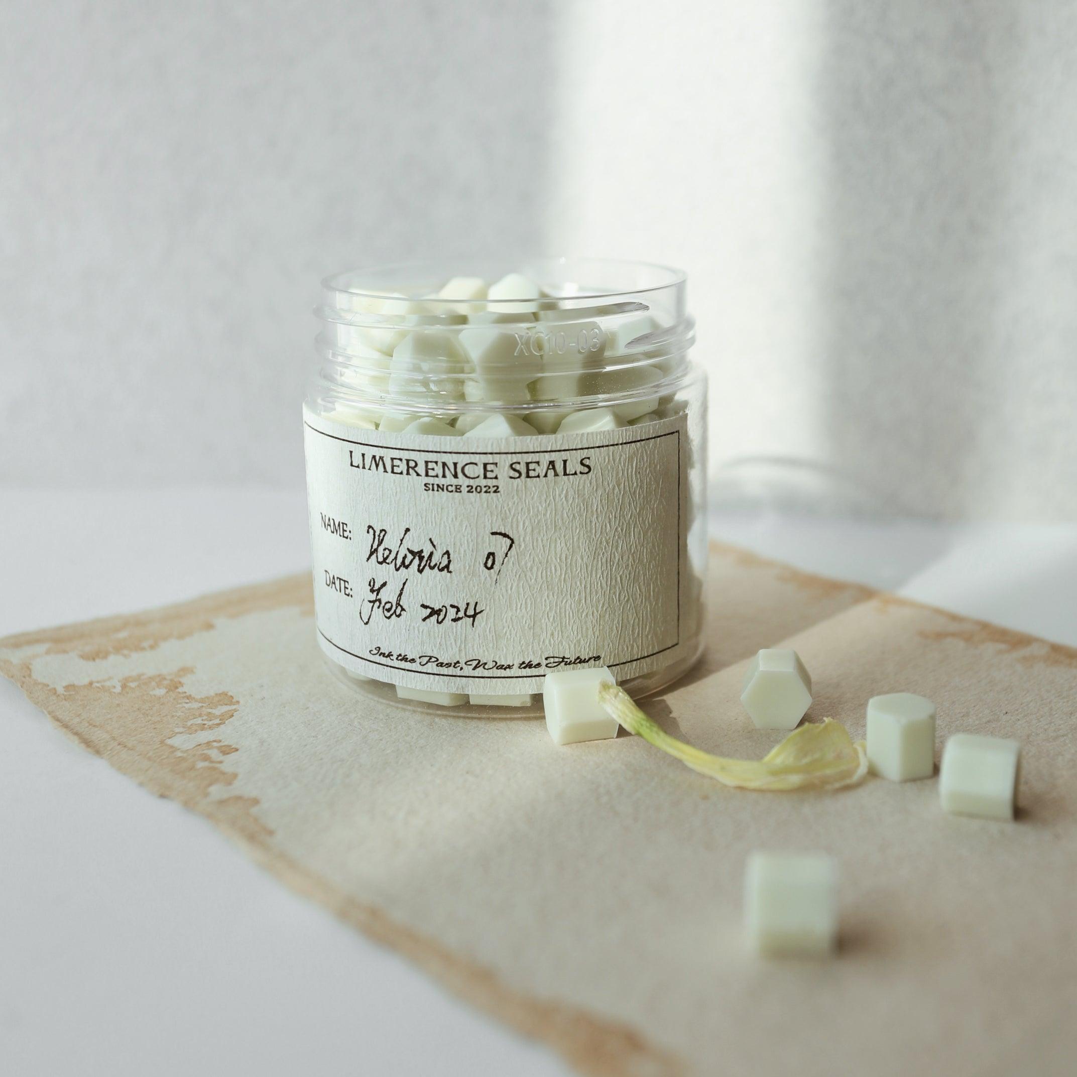 A jar of mint green Veloria handmade sealing wax beads by Limerence Seals, elegantly placed on a piece of textured parchment paper. The soft, natural lighting enhances the refreshing mint hue of the beads, making them ideal for adding a touch of sophistication to personalized letters and elegant gift presentations.