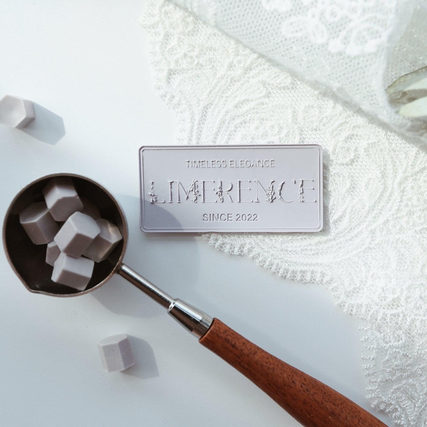 A violet Limerence Seals label embossed with "TIMELESS ELEGANCE - LIMERENCE - SINCE 2022," set beside a wooden-handled wax spoon filled with violet Veloria handmade sealing wax beads. The scene is accentuated with delicate lace, highlighting a blend of elegance and craftsmanship, ideal for personalizing letters and upscale gift wrapping.